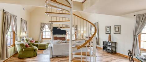 A spacious room with a spiral staircase, wooden flooring, a bed, a green armchair, and a desk with a lamp.