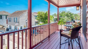 A wooden deck with a red railing, a wicker chair, and a table with a cushion.