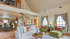 A spacious living room with a white sofa, green armchairs, and a wooden coffee table. A spiral staircase leads to an upper level.