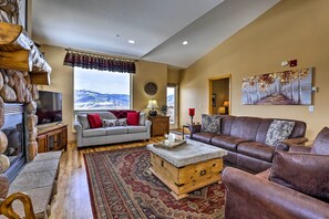 Ein gemütliches Wohnzimmer mit Kamin, einem großen Fenster mit Bergblick, einem braunen Ledersofa und einem gemusterten Teppich.