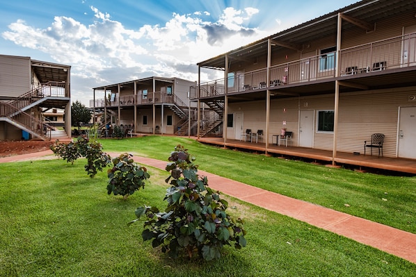 A multi-story hotel with outdoor seating areas and a well-maintained lawn. - Oasis at Newman (Newman)