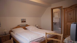 Un dormitorio con dos camas individuales, un armario de madera, una mesita con mantel rosa y una mesita de noche con lámpara.