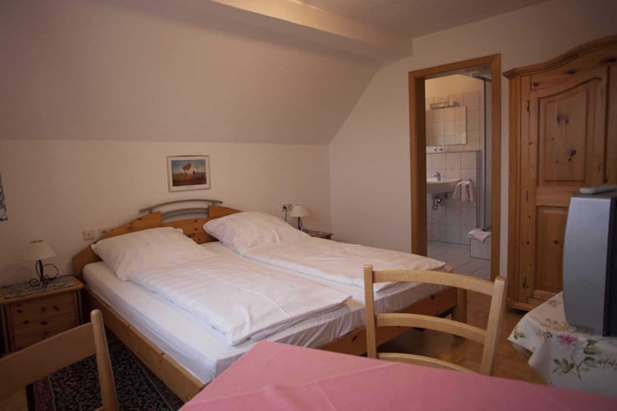 A bedroom with two single beds, a wooden wardrobe, a small table with a pink tablecloth, and a nightstand with a lamp.