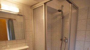 Un baño con ducha envuelta en vidrio, lavamanos y retrete.