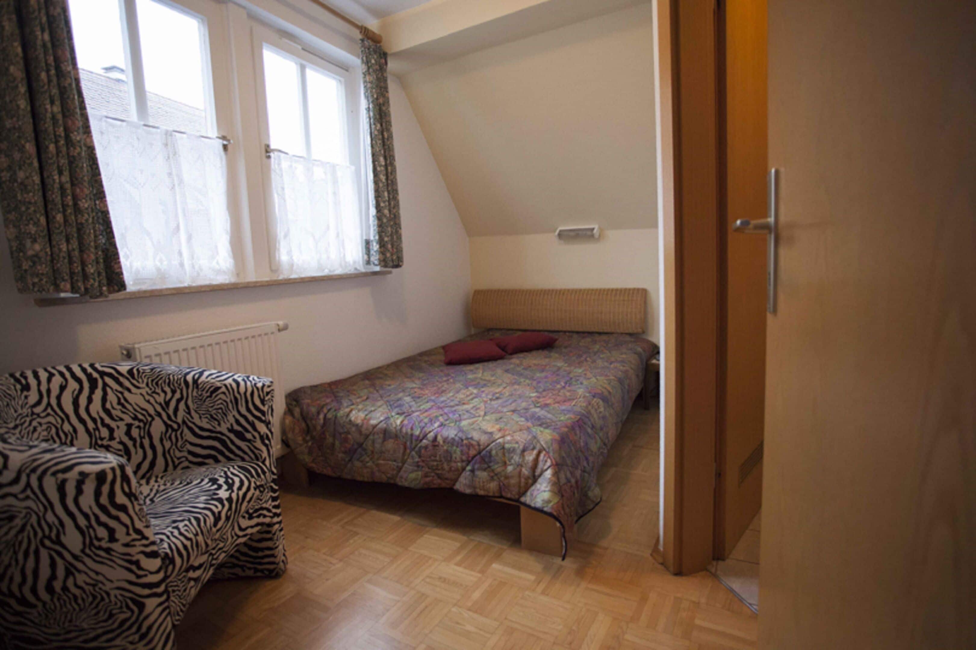 A bedroom with a bed, a zebra-patterned chair, and a window with curtains.