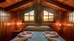 Une chambre dans une cabane en bois, avec un lit, deux fenêtres et un plafond en bois.