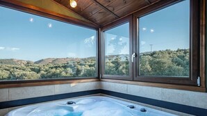 Un bain à remous avec vue sur un paysage vallonné, grâce à de grandes fenêtres.