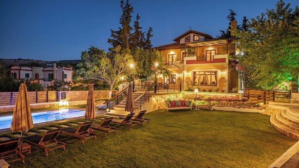 Une maison à deux étages avec une piscine, un espace salon extérieur et un jardin bien éclairé.