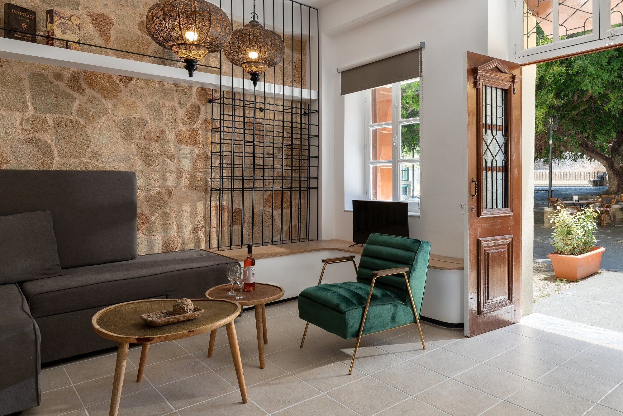 Una sala de estar moderna con una pared de piedra, un sofá, un sillón verde, una mesa de centro y dos lámparas colgantes.