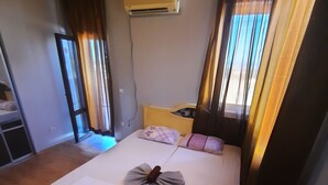 A room with a bed, a window with blinds, a wall-mounted air conditioner, and a door leading to another room. - Beautiful 2-bed Villa in Cholakova Cheshma (Kosharitsa)