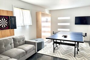 A modern living room with a dartboard, a sofa, a table tennis table, and a TV mounted on the wall.