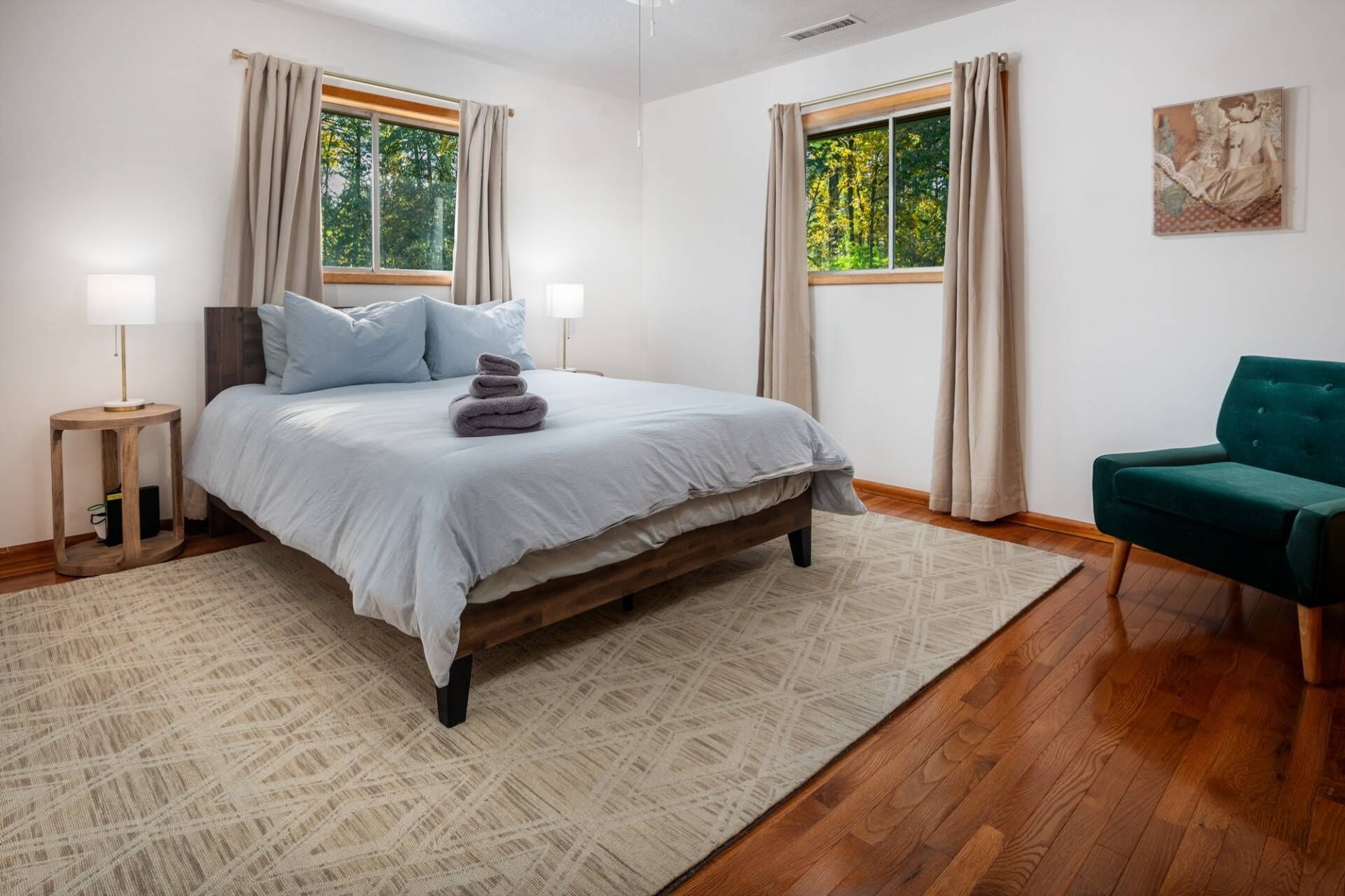 Une chambre à coucher avec un lit, deux lampes de chevet, un fauteuil vert et un tableau accroché au mur.