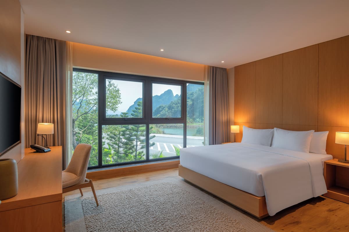 Quarto de hotel com uma janela grande, uma cama, uma escrivaninha e uma cadeira.