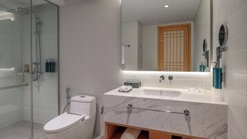 Un baño moderno con ducha de vidrio, inodoro blanco, lavamanos de mármol y tocador de madera.