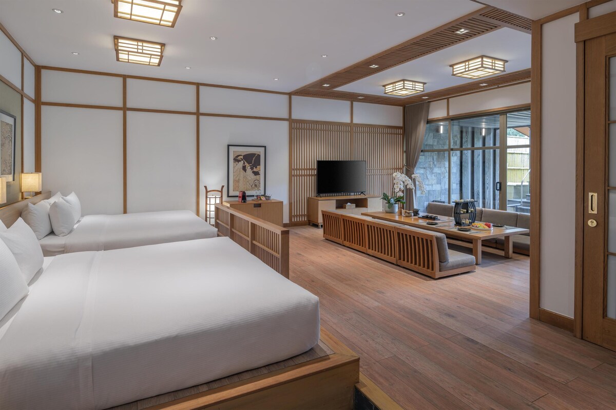 Habitación de hotel con una cama grande, televisión, zona de estar con una mesa y puerta corrediza de vidrio al exterior.