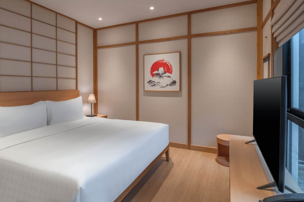 Quarto de hotel com cama, televisão, obra de arte na parede e janela.