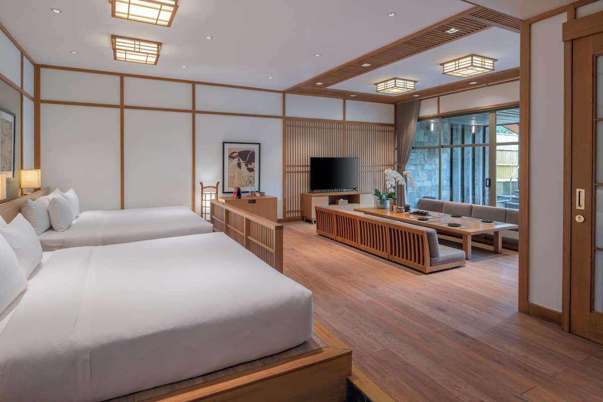 Quarto de hotel moderno com uma cama grande, televisão, área de estar e porta de vidro deslizante para o exterior.