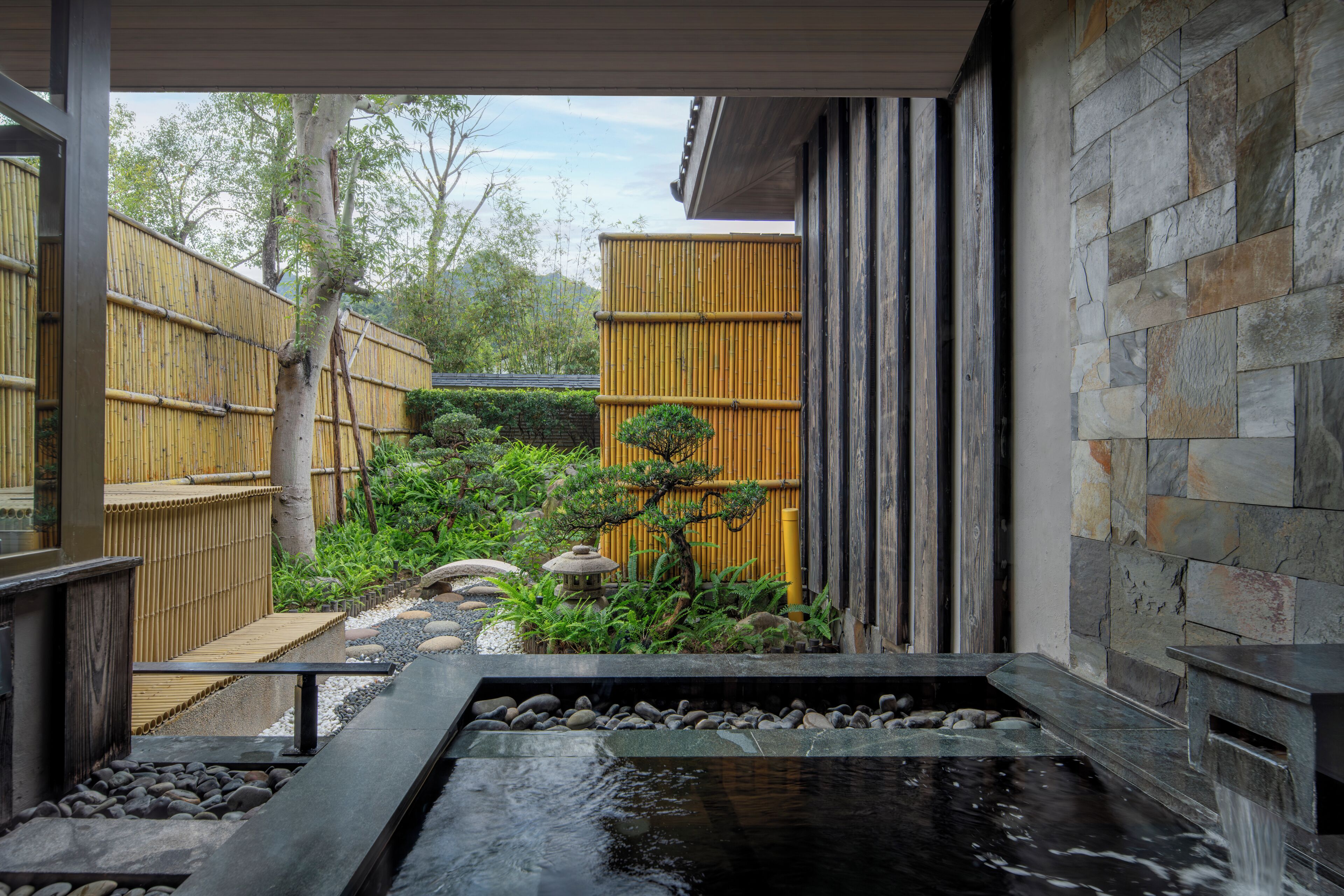 Een traditionele Japanse tuin met een vijver met koi karpers, een bamboebescherming en een stenen muur.