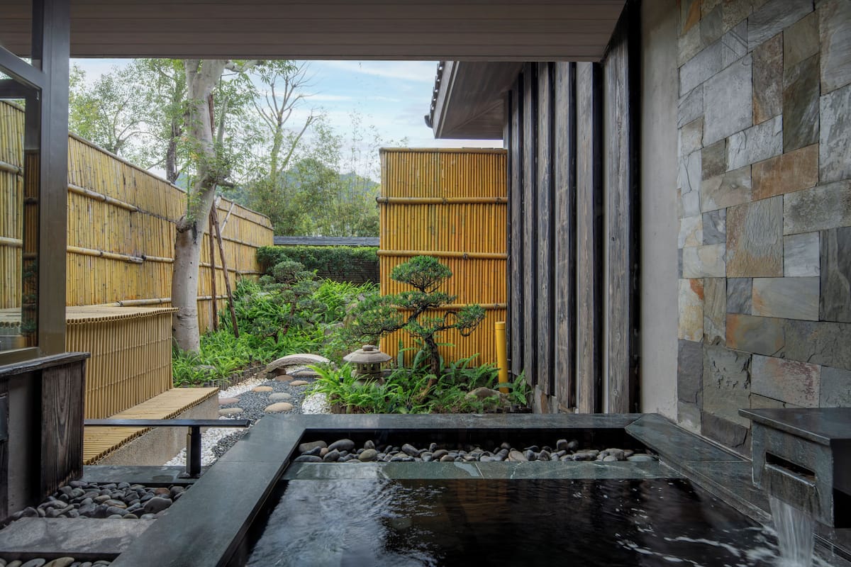 Um jardim japonês tradicional com lago de carpas, cerca de bambu e parede de pedra.