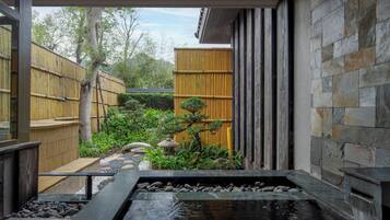 Un jardín japonés tradicional con un estanque de carpas koi, valla de bambú y muro de piedra.