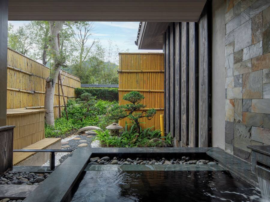 Un jardín japonés tradicional con un estanque de carpas koi, valla de bambú y muro de piedra.