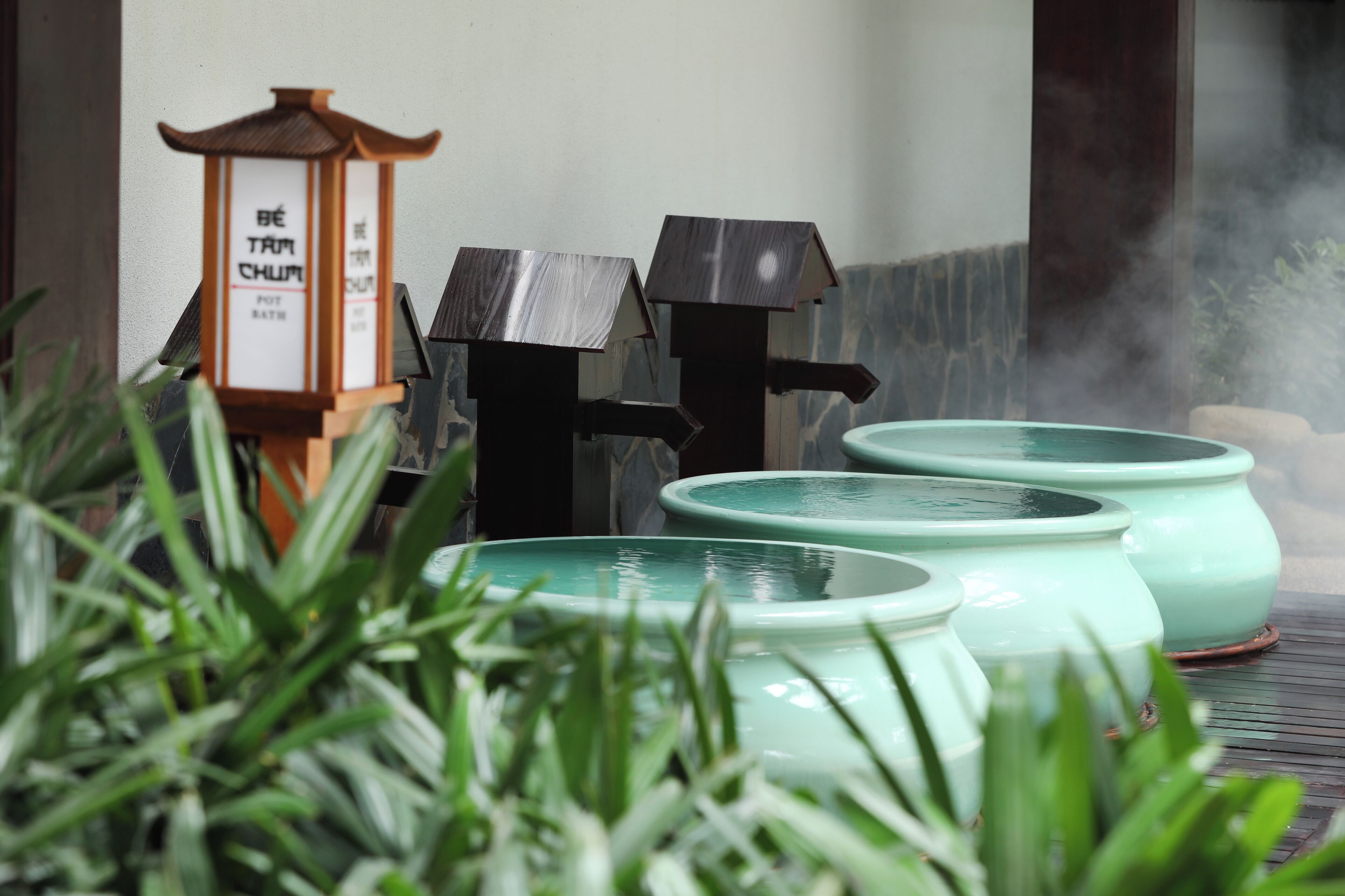 A traditional Japanese tea house with a bamboo water heater, a lantern, and a stone wall.