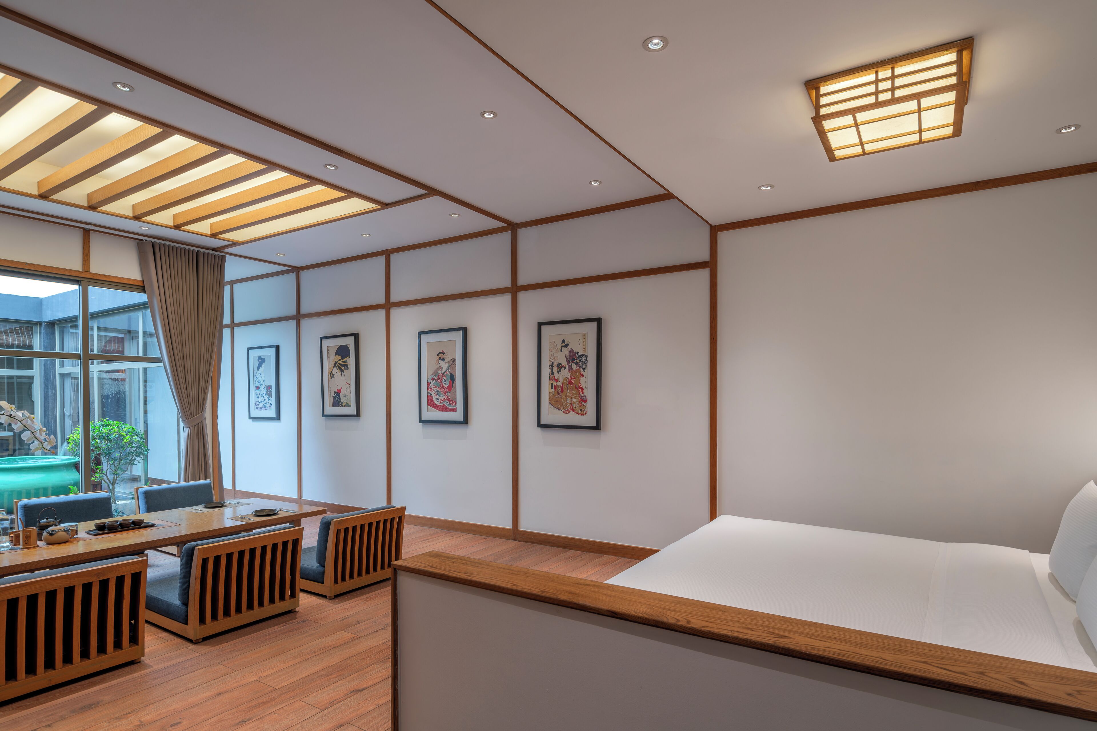 A modern hotel room with a wooden floor, a large bed, a dining table with chairs, and artwork on the walls.