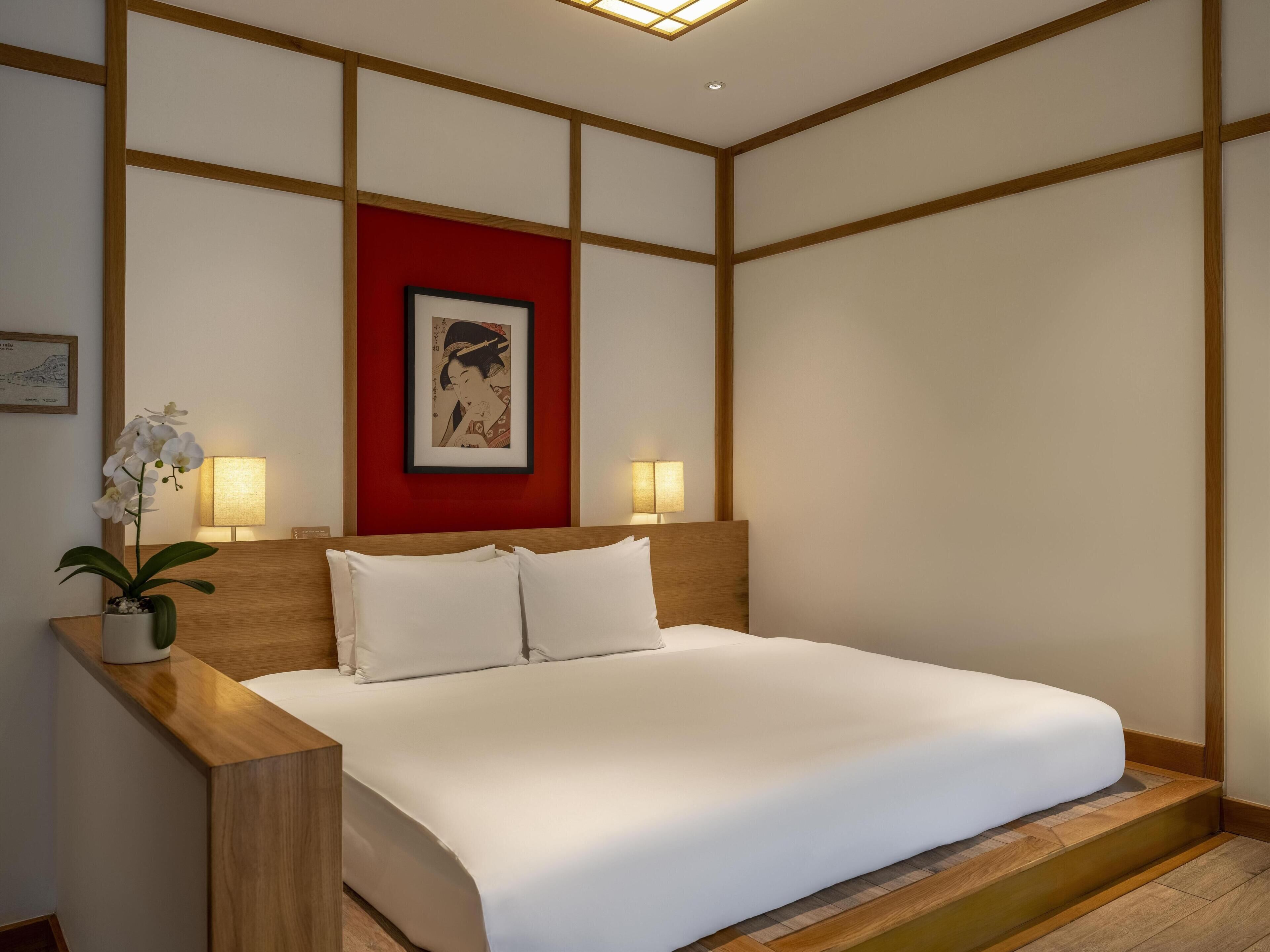A hotel room with a bed, bedside lamps, a red accent wall, and a framed artwork.