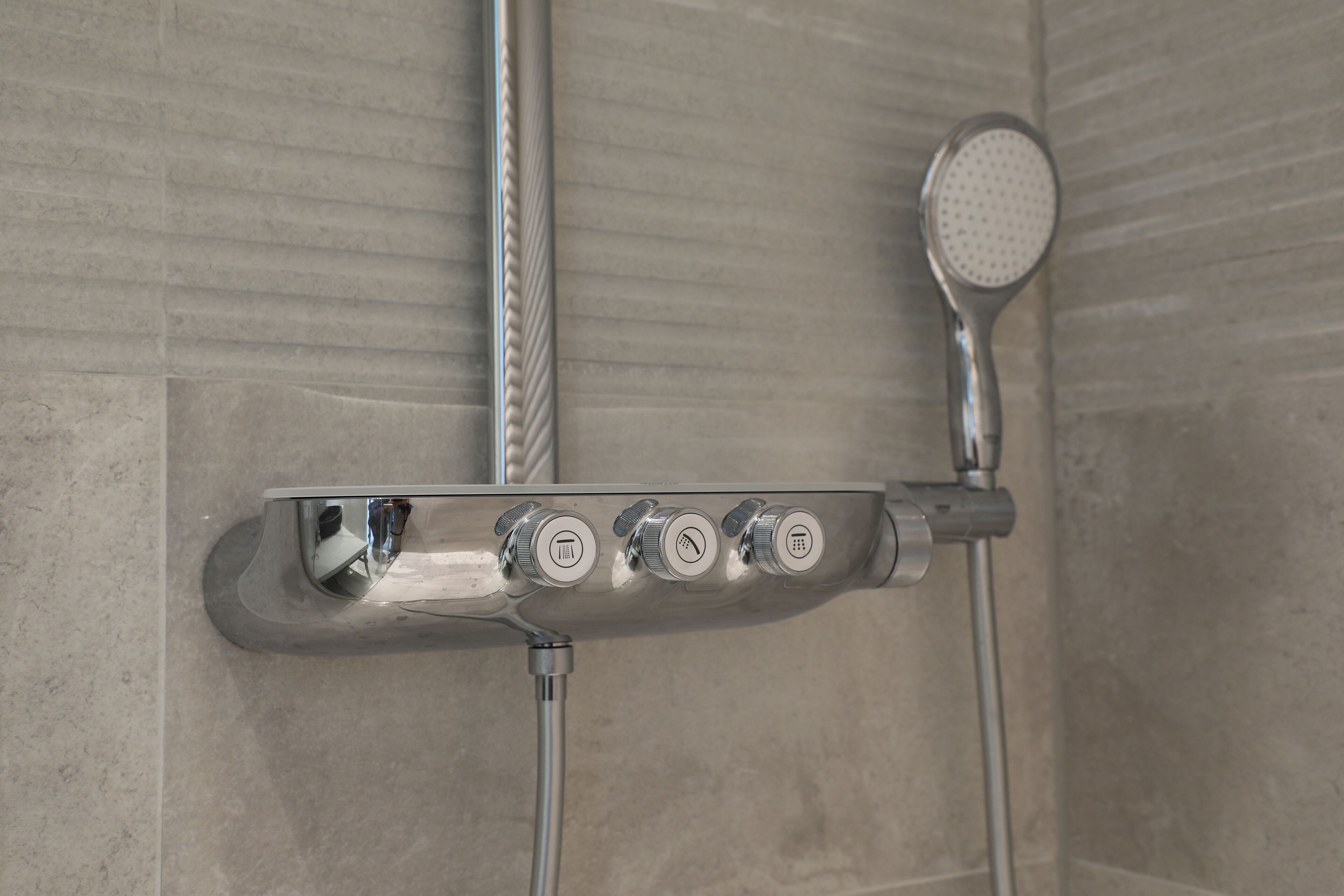Chuveiro com chuveiro manual e painel de controle fixado na parede com várias opções.