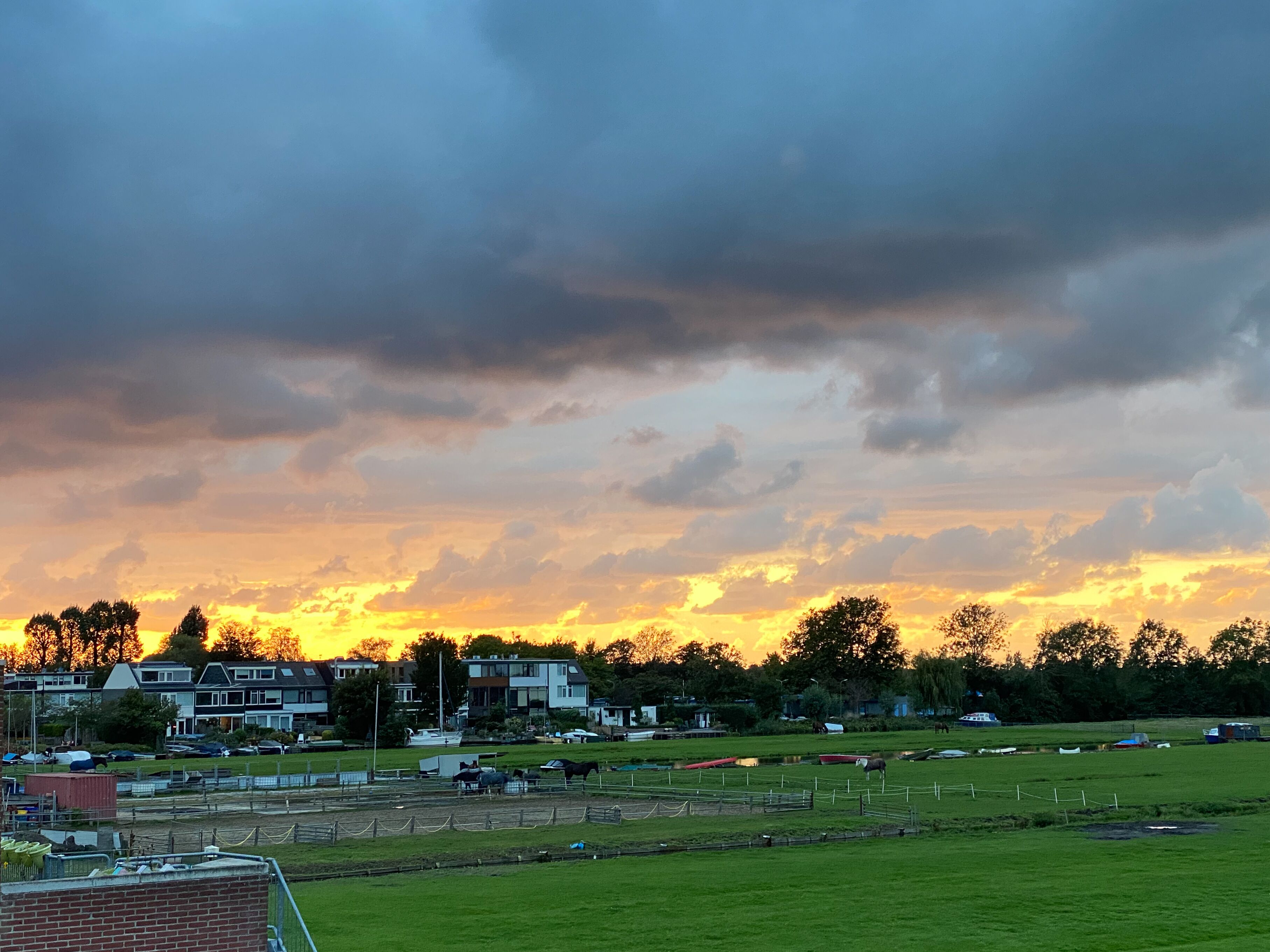 A rural landscape with a field, a few buildings, and a cloudy sky.