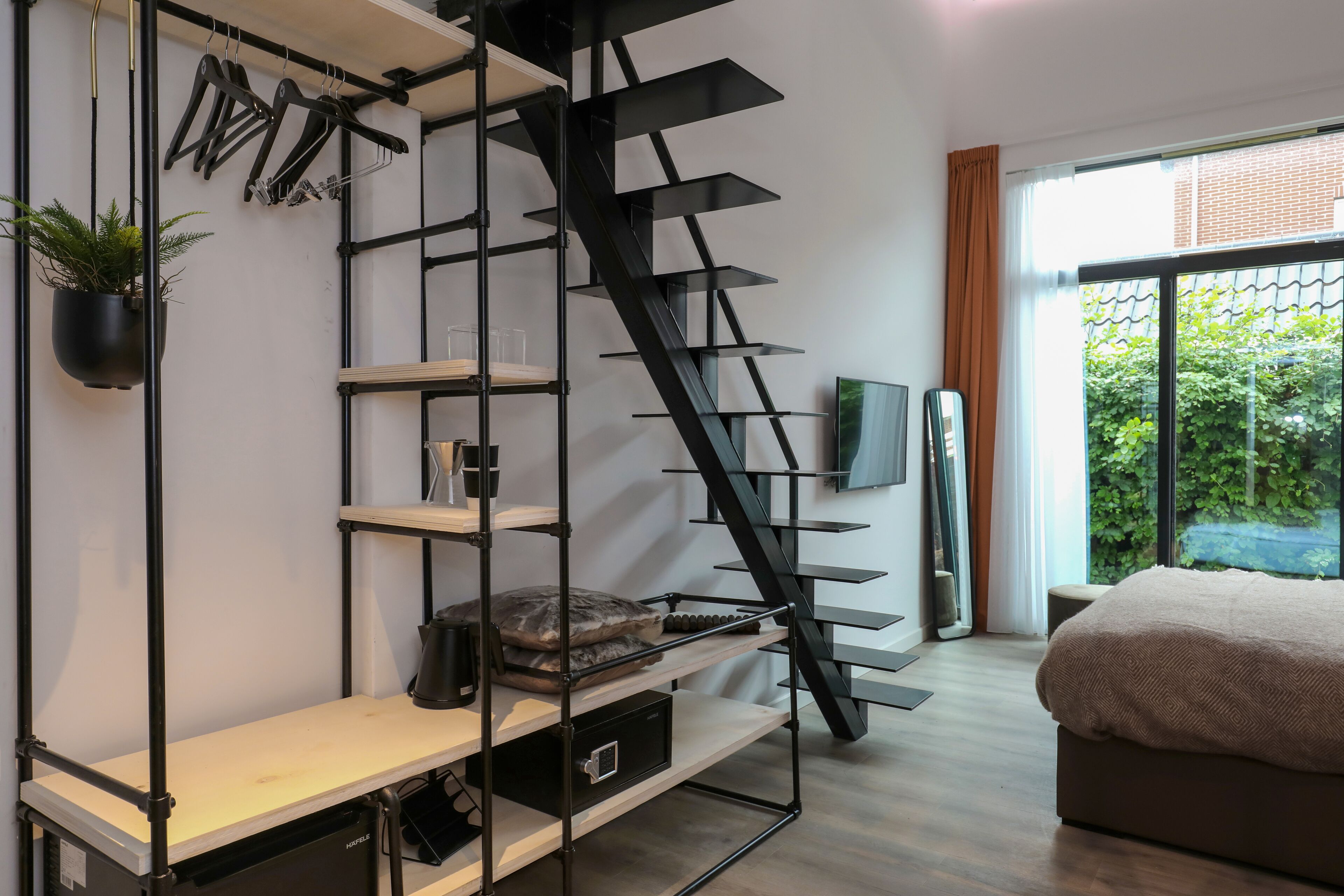 A modern bedroom with a built-in staircase, a bed, a TV, and a window with a view of greenery.