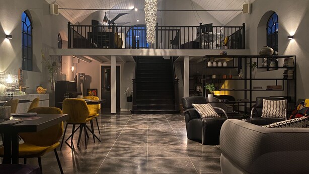 A spacious living area with a high ceiling, a staircase leading to an upper level, and a dining area with yellow chairs. - Valerius Boutique Hotel (Wormer)