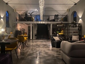 A spacious living area with a high ceiling, a staircase leading to an upper level, and a dining area with yellow chairs. - Valerius Boutique Hotel (Wormer)