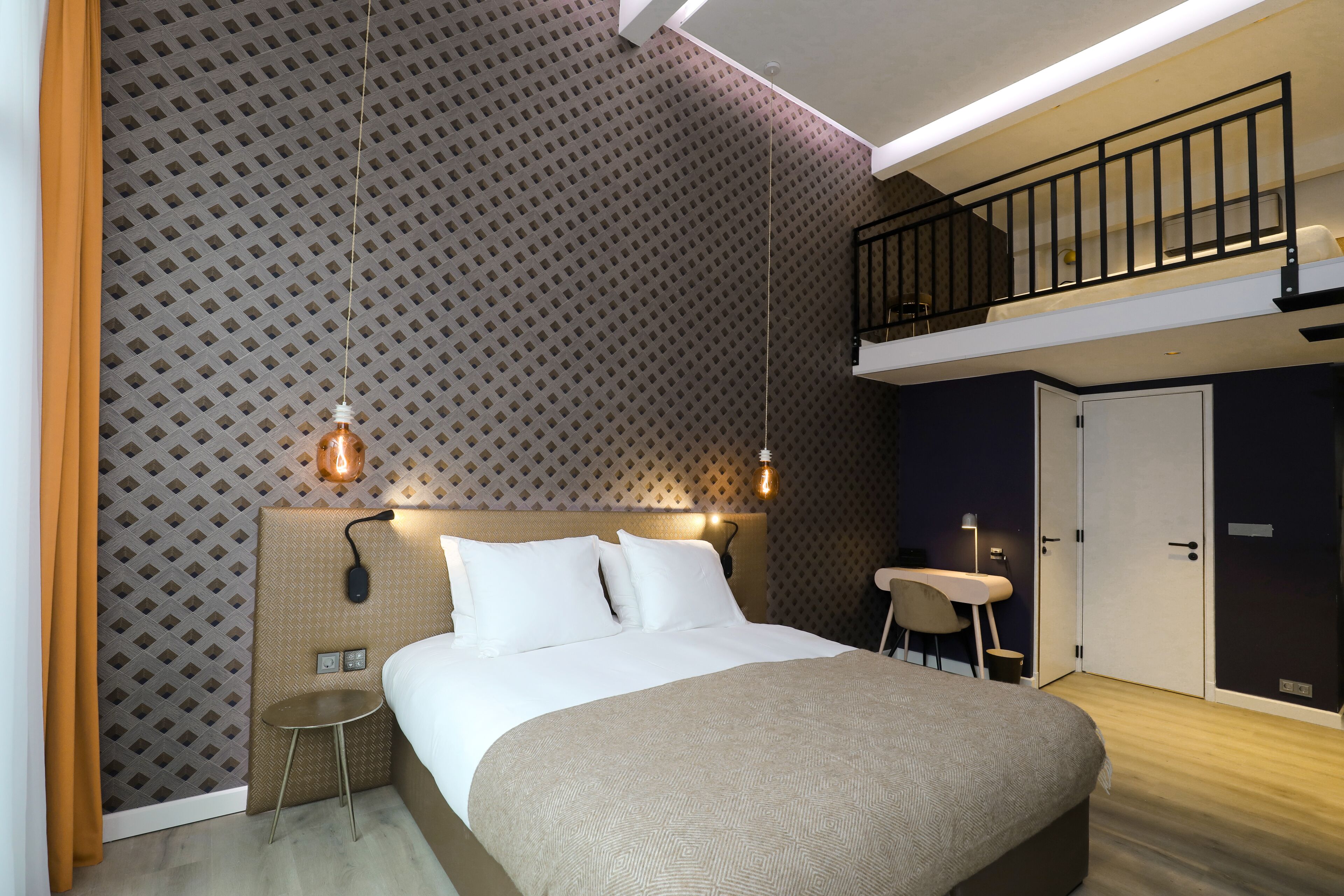 Une chambre d’hôtel moderne avec un grand lit, une petite table, une chaise et un balcon doté d’une rambarde.