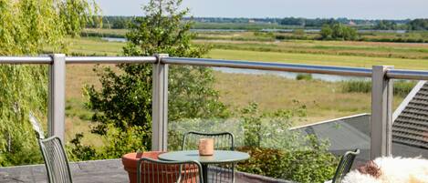 A balcony with a table and chairs, overlooking a river and fields.