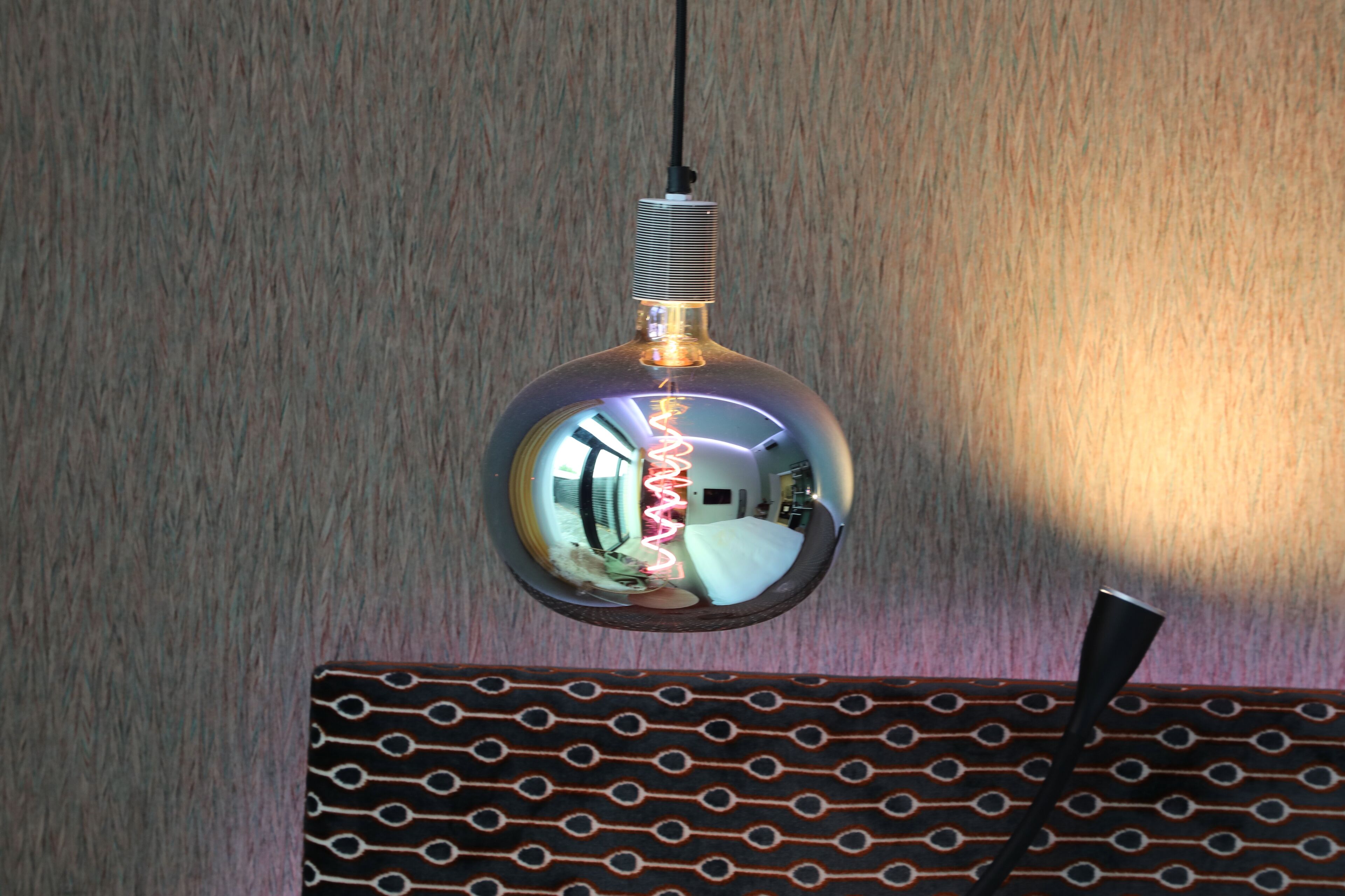 Een bolvormige hanglamp met een metalen afwerking, die de omgeving weerspiegelt.