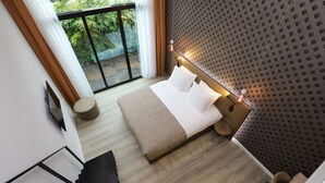 A modern hotel room with a large bed, a small round table, a sofa, and a view of greenery through a sliding door. - Valerius Boutique Hotel (Wormer)