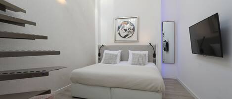 Un dormitorio moderno con cama, televisor de pantalla plana, una obra de arte enmarcada y estanterías empotradas.