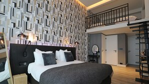 A modern bedroom with a large bed, a black headboard, a geometric patterned wall, a small balcony, and a wooden floor. - Valerius Boutique Hotel (Wormer)