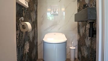 A modern bathroom with a toilet, a paper towel holder, and a wall-mounted light switch.