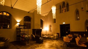 A spacious interior with a high ceiling, hanging chandeliers, a fireplace, and a seating area with sofas and chairs. - Valerius Boutique Hotel (Wormer)
