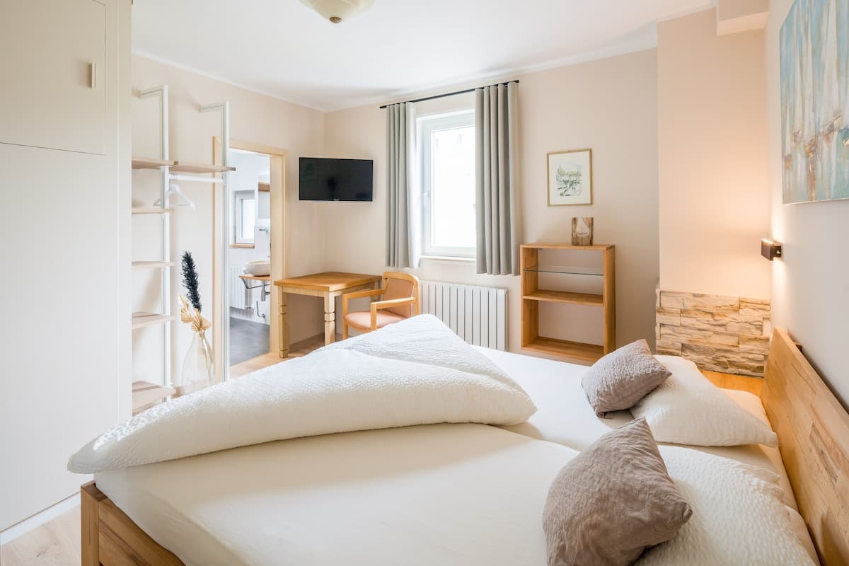 A bedroom with a bed, pillows, a desk, a chair, a television, and a window with curtains.