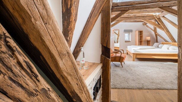 A bedroom with a wooden ceiling, a bed, a chair, and a small table with a bottle and glasses. - Landhotel Löwen (Erlabrunn)