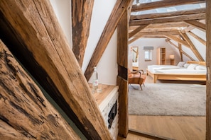 A bedroom with a wooden ceiling, a bed, a chair, and a small table with a bottle and glasses. - Landhotel Löwen (Erlabrunn)