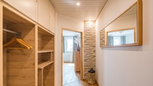 A hallway with wooden flooring, a stone accent wall, and a mirror on the right. - Landhotel Löwen (Erlabrunn)