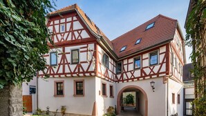 A traditional half-timbered building with a central archway, a paved courtyard, and a small bench. - Landhotel Löwen (Erlabrunn)