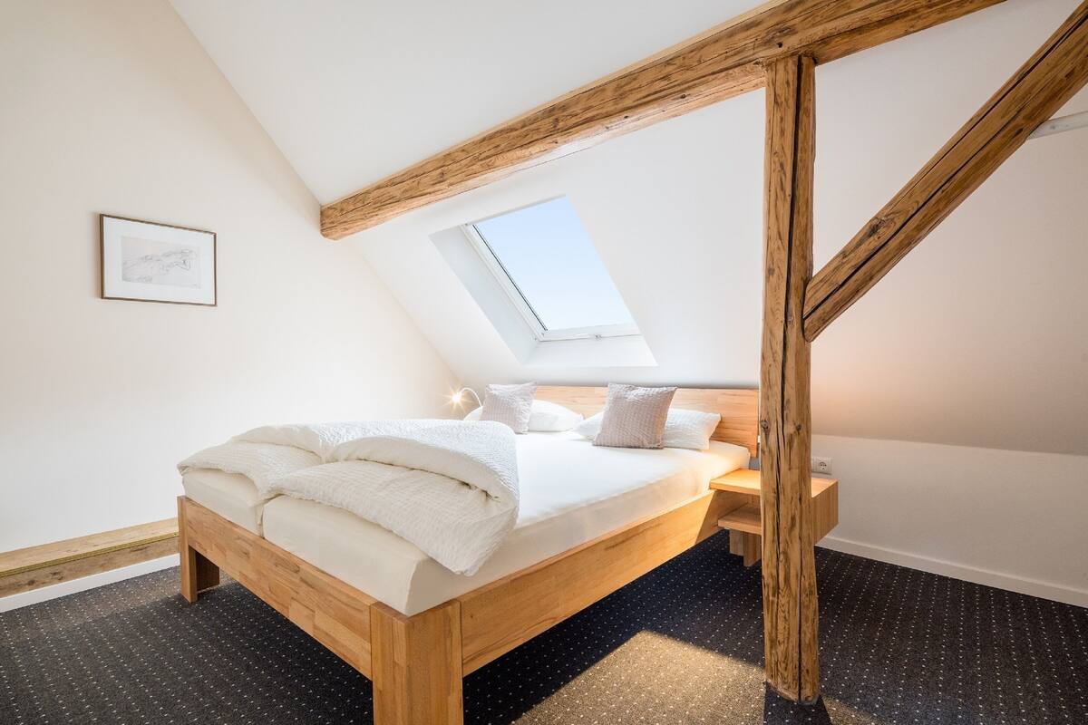 A bedroom with a sloped ceiling, a skylight, a wooden bed frame, and a small bedside table.