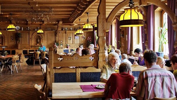 Una posada tradicional con interiores de madera, mesas de comedor compartidas y lámparas amarillas colgantes.
