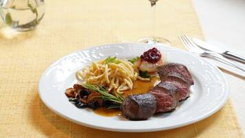 A plate of food with pasta, meat, and a glass of red wine on a table.