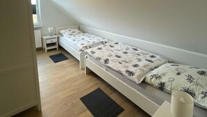 A small, single-bed room with a sloped ceiling, a bedside table with a lamp, and a window providing natural light. - Haus Landruhe, Deutschland (Neuharlingersiel)